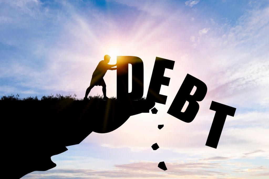 silhouette of a man pushing big letters that spell "debt" off a cliff