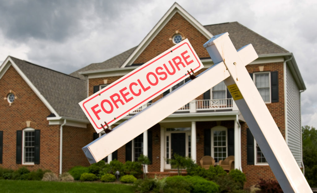white wooden foreclosure sign in front of a modern brick house