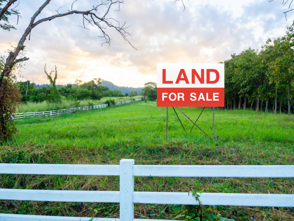 white wooden fence around a lot of green grass with a red "Land For Sale" sign
