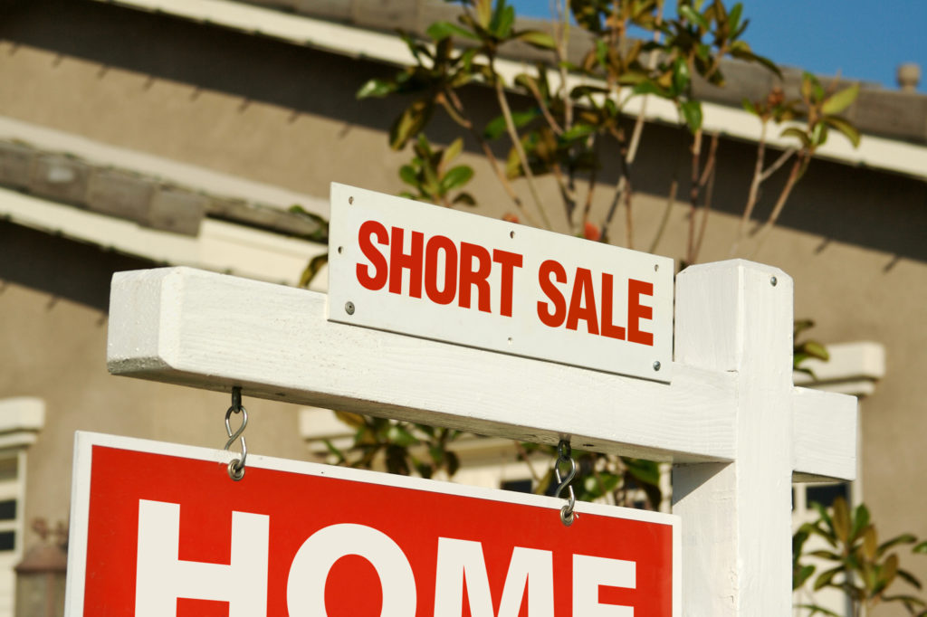 white wooden sign with red letters that say "short sale"